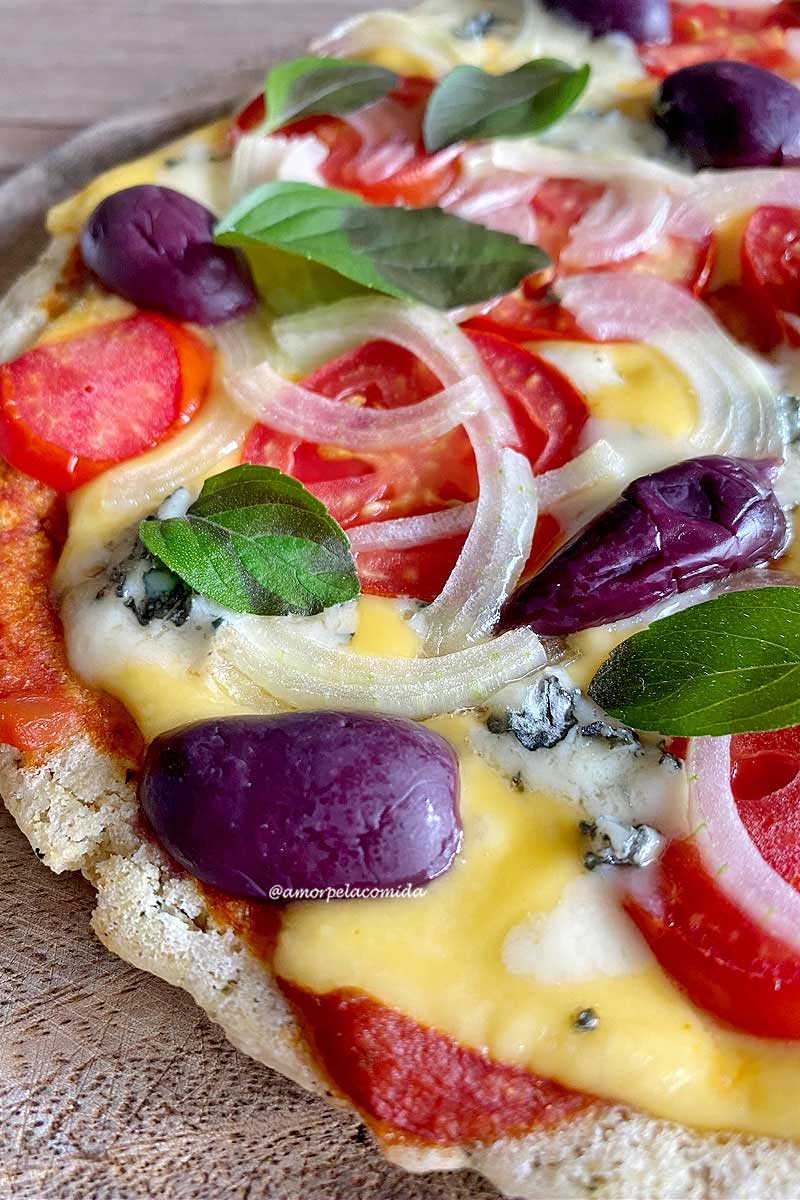 Pizza sobre tábua de madeira, na cobertura queijo, tomate, cebola, manjericão e azeitonas pretas