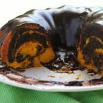 Bolo de cenoura mesclado com chocolate partido sobre prato de bolo branco com cobertura cremosa de chocolate